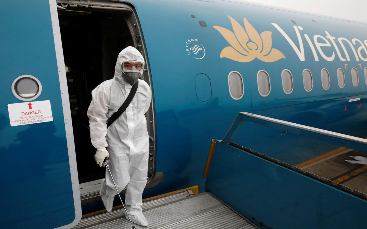 A health worker sprays disinfectant inside an Vietnam Airlines plane, the employer of the British pilot who is now in intensive care in Vietnam - Reuters