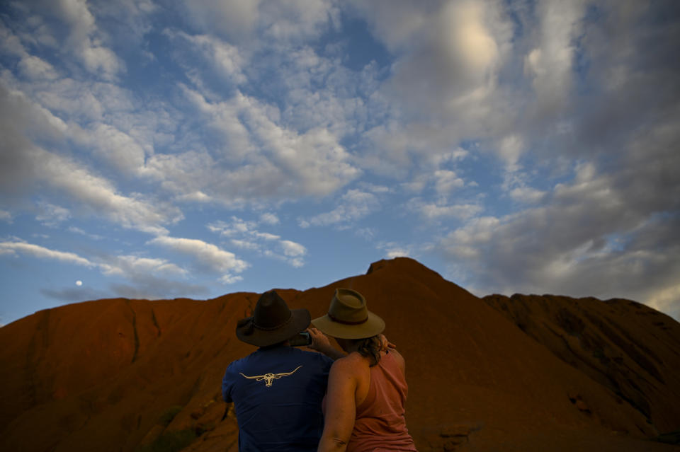 Picture of two tourists looking ay Uluru from the bottom and taking a photo