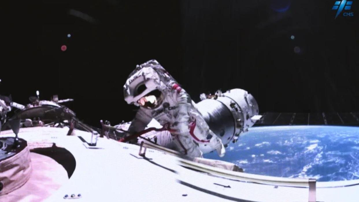  An astronaut in a spacesuit floats outside of a large white cylinder in space. earth can be seen in the background. 