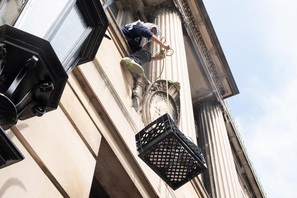 A person dangles a milk crate out of a Hamilton Hall window. 