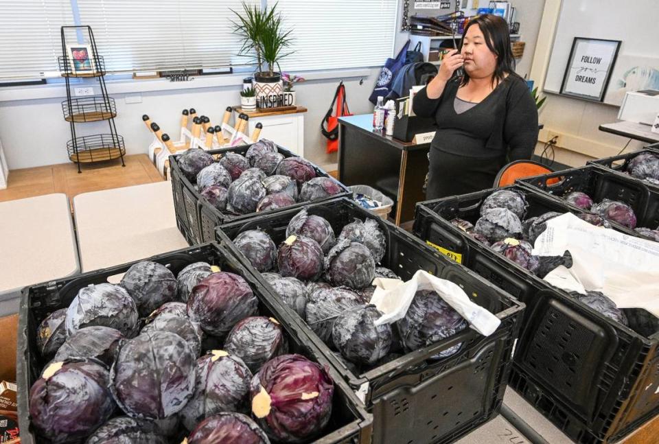 Fort Miller Middle School Community School coordinator Xee Xiong radios the office while standing in front of bins of donated cabbages during the Fresno school’s Food Pantry & Clothing Closet event at the Fresno school on Friday, March 8, 2024. CRAIG KOHLRUSS/ckohlruss@fresnobee.com