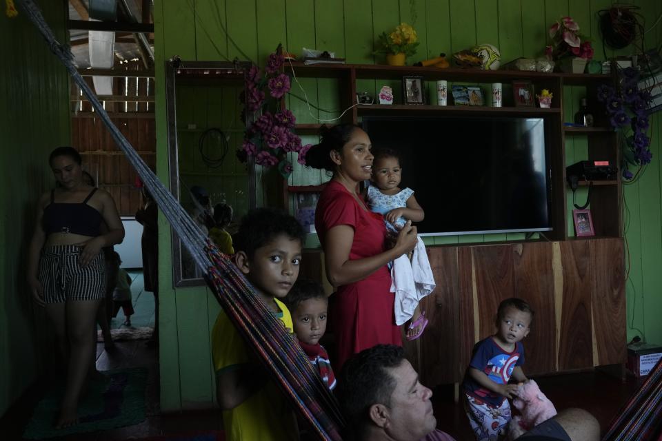 Fernanda de Araujo Moraes, center, president of the local riverine association, holds a child at her home in Lago Serrado community, near Carauari, Brazil, Thursday, Sept. 1, 2022. A Brazilian non-profit has created a new model for land ownership that welcomes both local people and scientists to collaborate in preserving the Amazon. To involve the riverine communities in governance, the institute set up a steering committee and launched a series of public meetings called "community of dreams," where people can prioritize the improvements they want most. (AP Photo/Jorge Saenz)