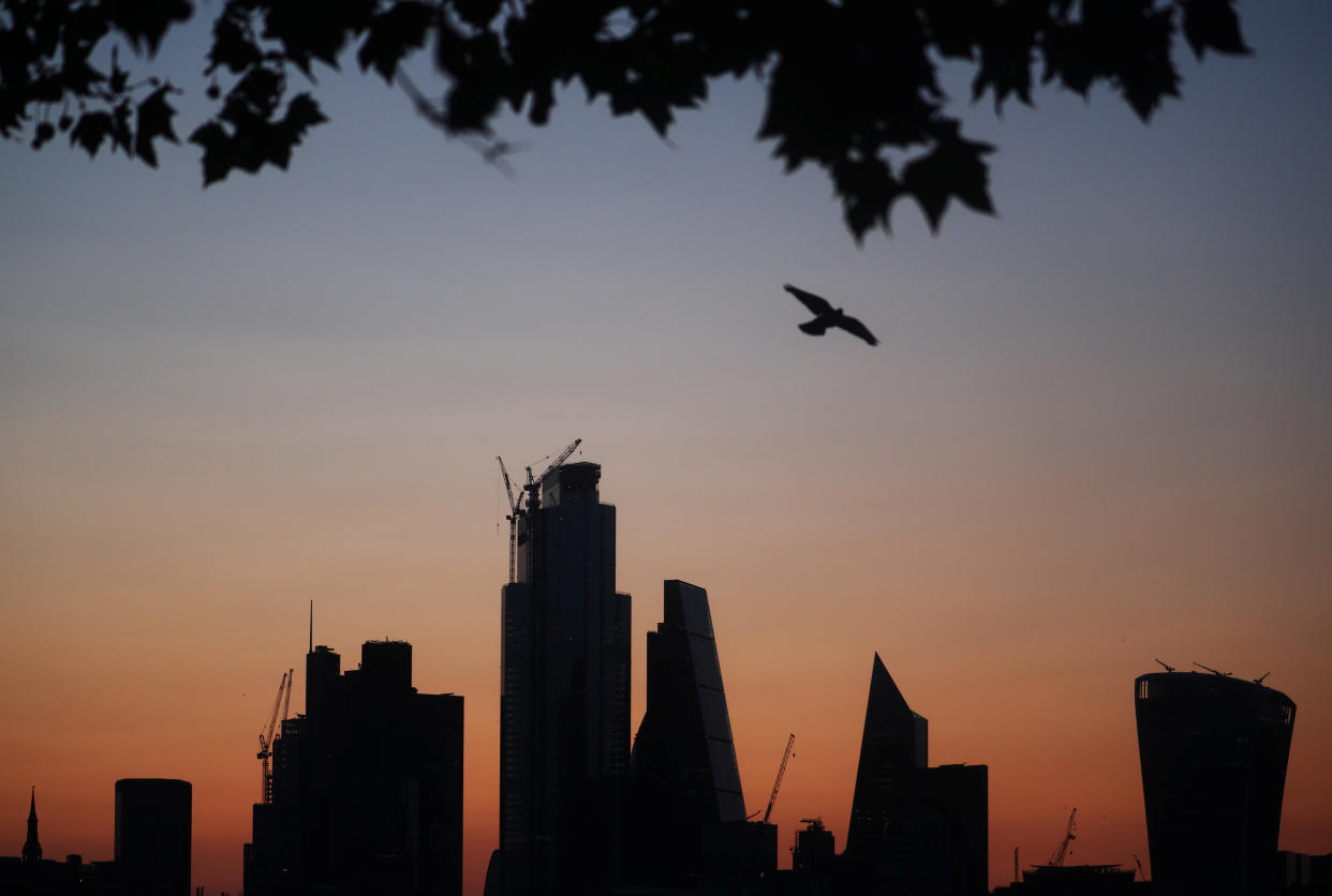 A bird flies as the sun rises behind the city of London financial district in London, Britain August 20, 2019. REUTERS/Hannah McKay