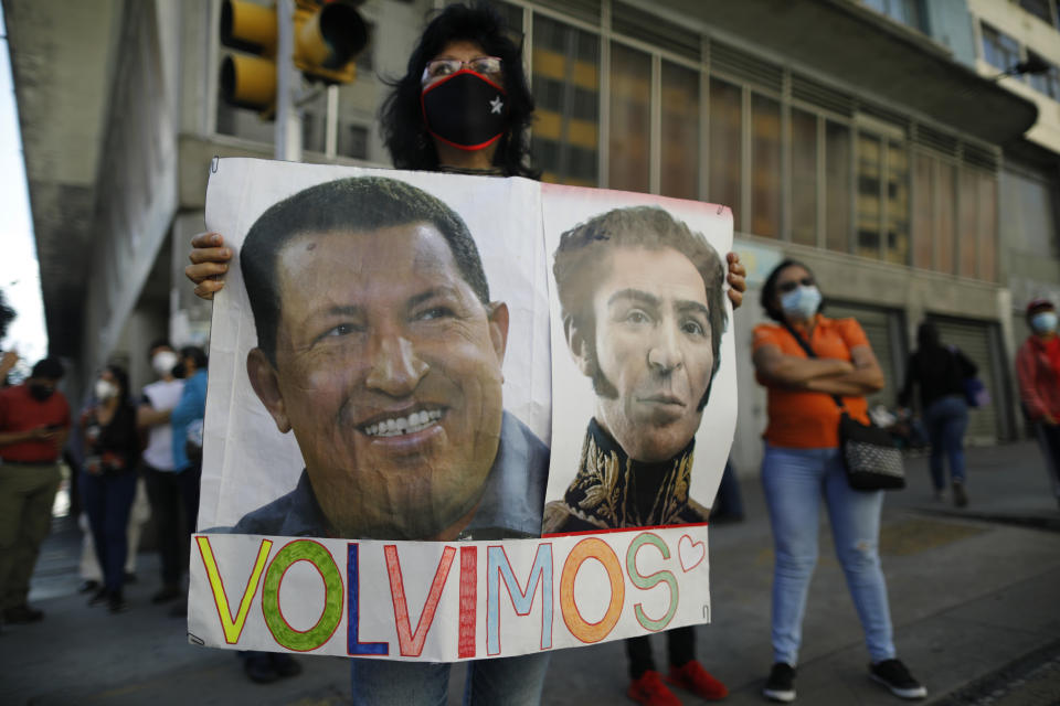 A government supporter holds photos of late Venezuelan President Hugo Chavez, left, and independence hero Simon Bolivar with the Spanish message "We're back" outside the National Assembly where lawmakers are being sworn-in, in Caracas, Venezuela, Tuesday, Jan. 5, 2021. The ruling socialist party assumed the leadership of Venezuela's congress on Tuesday, the last institution in the country it didn't already control. (AP Photo/Ariana Cubillos)