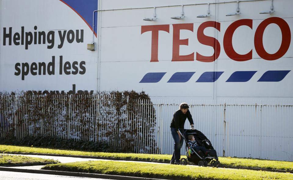 A man pushes a pram past a Tesco supermarket near Altrincham, northern England, April 22, 2015. Tesco plunged to an annual loss of 6.4 billion pounds ($9.5 billion) on Wednesday, the worst in its 96-year history, after shoppers deserted Britain's biggest retailer and forced it to write down the value of its stores. REUTERS/Phil Noble