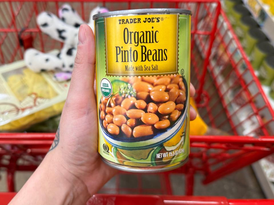 hand holding up a can of organic pinto beans over a cart at trader joes