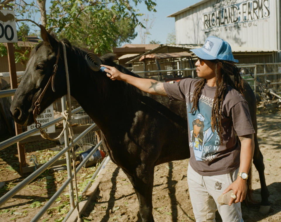 A Compton Cowboy next to a horse on a ranch wearing the Stevenson Ranch x Snoop Dogg collab t-shirt and hat. 