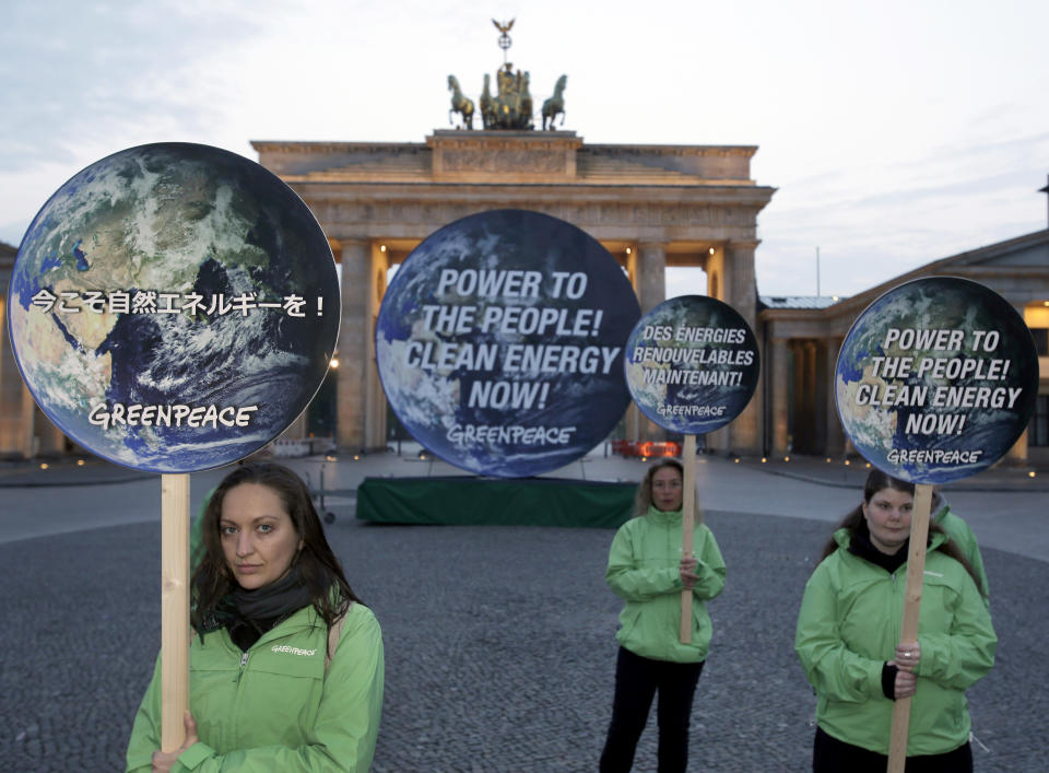 Activists of the international environmentalist organization Greenpeace pose with posters in front of the Brandenburg Gate in Berlin, Germany, Sunday, April 13, 2014, to support clean energy. After a one week meeting of the Intergovernmental Panel on Climate Change in Berlin the final document which is released on Sunday is expected to say that a global shift to renewable energy from fossil fuels like oil and coal are required to avoid potentially devastating sea level rise, flooding, droughts and other impacts of warming. (AP Photo/Michael Sohn)