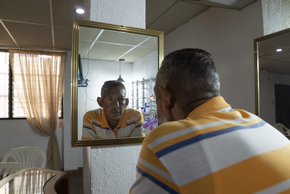 Jorge Montaño looks at himself in a mirror as he poses for a portrait at the office where he works repairing glasses and assisting an optomatrist in Caracas, Venezuela, Thursday, Feb. 23, 2023. Montaño, 51, who lives with his mother and three siblings at an apartment in Caracas. (AP Photo/Ariana Cubillos)