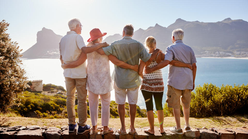 Rear View Of Senior Friends Visiting Tourist Landmark On Group Vacation Standing On Wall.