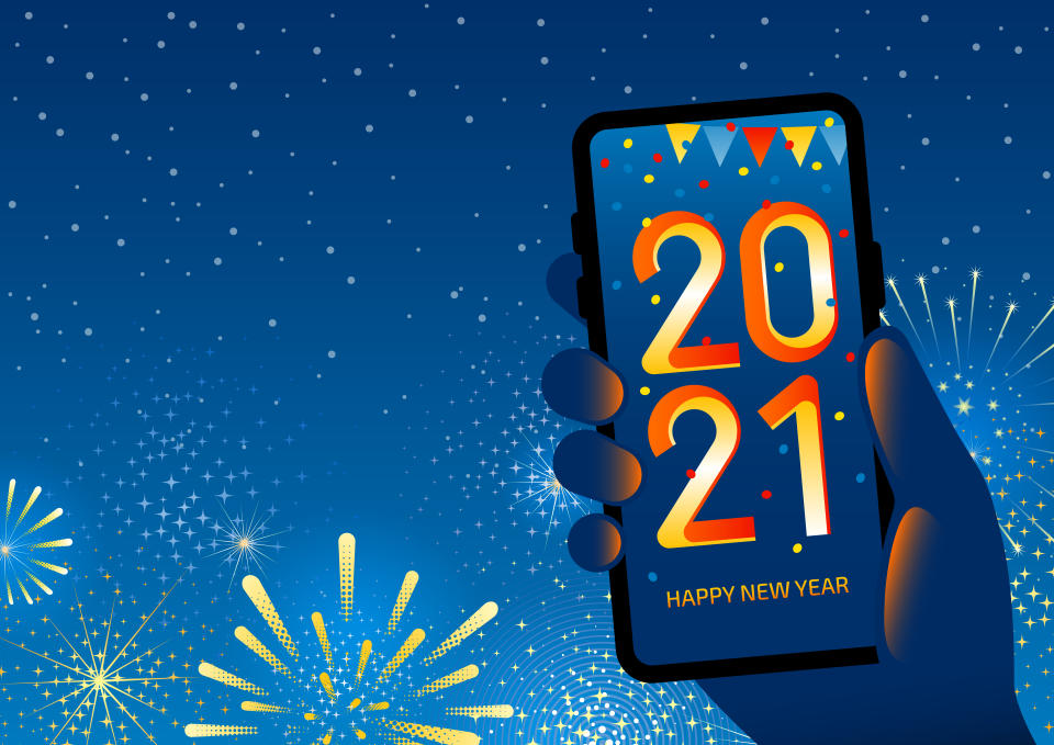 Hand holding a smartphone which displays a 2021 Happy New Year with confetti and decoration. Celebration with fireworks is in the background. There is space for your text, message.