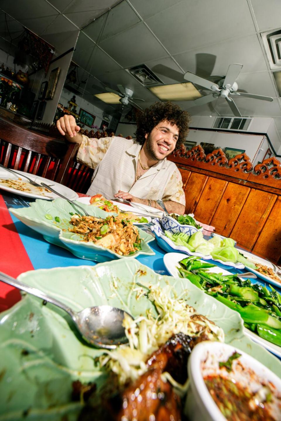 Benny Blanco surrounded by plates of food at Spicy BBQ Restaurant.