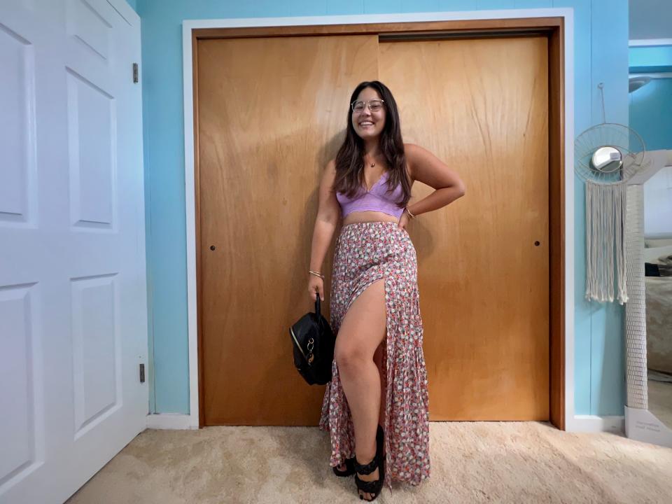 Author posing with purple crop-top, purple, patterned long skirt, black backpack, and black sandals.