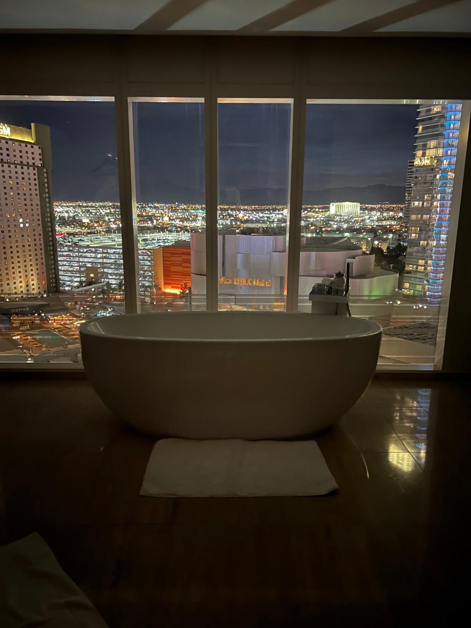 A standalone soaking tub at night with the city skyline behind it.