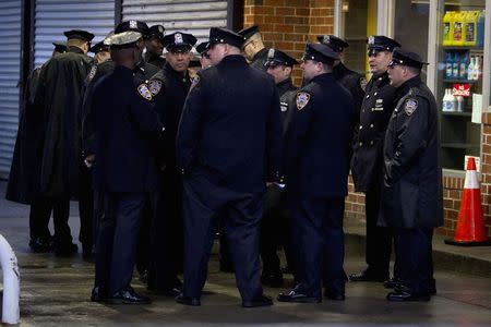 Police officers stand under a gas station roof to stay out of the rain, before slain New York Police Department officer Wenjian Liu's funeral in the Brooklyn borough of New York January 4, 2015. REUTERS/Carlo Allegri