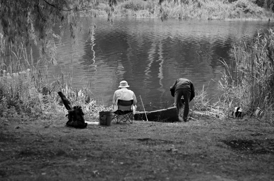 Two people at the edge of a pond fishing.