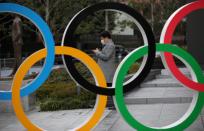 FILE PHOTO: Man wearing protective face mask looks at his mobile phone next to The Olympic rings in front of the Japan Olympics Museum in Tokyo