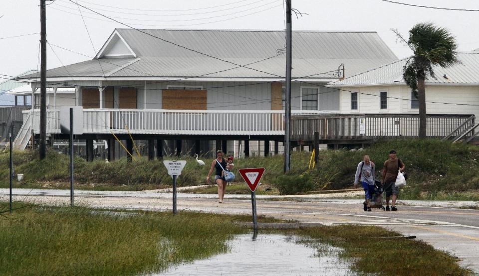 Residents carry belongings from the west end of the island as the roads are closed from 3-4 feet of sand covering the road in Dauphin Island, Ala. on Thursday, Aug. 30, 2012. Isaac dumped as much as 4 feet of sand on roads on Dauphin Island, but damage isn't bad otherwise. Mayor Jeff Collier said Thursday no homes were destroyed on the coastal barrier, even at its vulnerable western end. Crews in tractors are moving sand off the streets. Collier says conditions may have been worse without a 3.5-mile-long sand pile that was built during the BP oil spill. He says the berm helped stop sand that would have wound up on streets and in sewers without it. (AP Photo/Butch Dill)