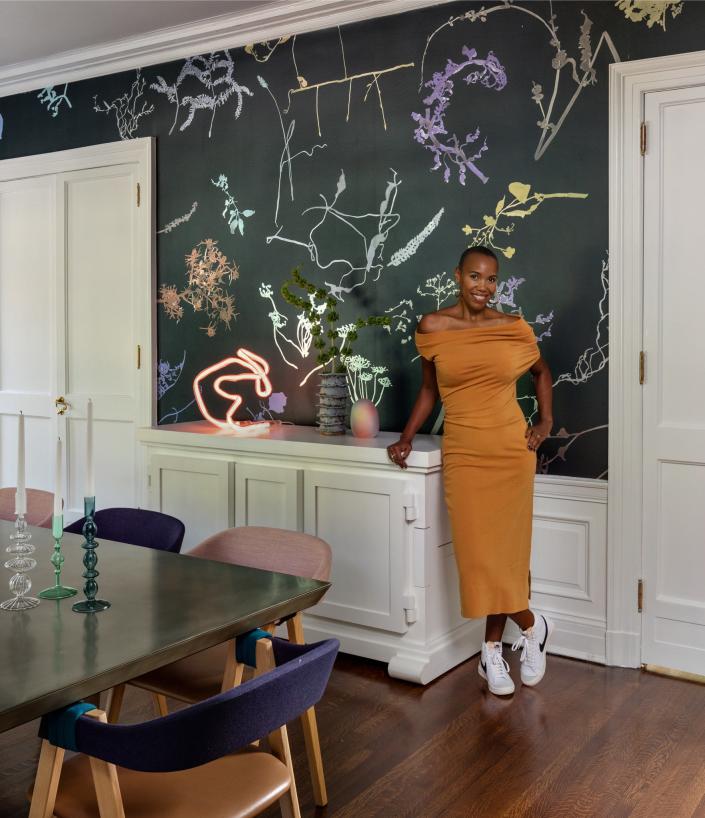 Designer Danielle Fennoy stands in the dining room next to a <a href="https://www.thefutureperfect.com/product/uncategorized/neon-table-lamp-pink-helium/" rel="nofollow noopener" target="_blank" data-ylk="slk:Jochen Holz neon table lamp." class="link ">Jochen Holz neon table lamp.</a>