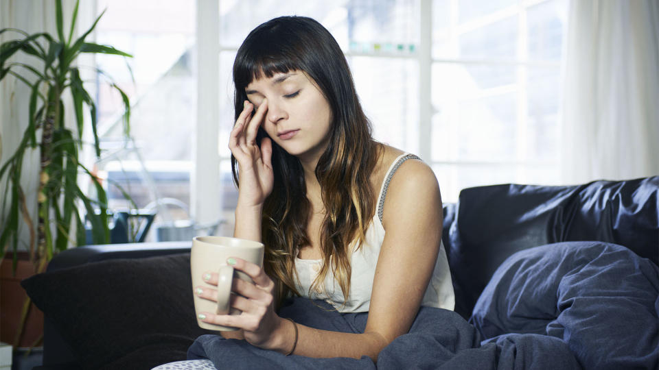 A woman sits up in bed looking tired holding a cup of coffee