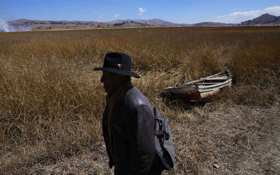 An Aymara man walks past an abandoned boat near the shore of Lake Titicaca in Huarina, Bolivia, Thursday, July 27, 2023. The lake's low water level is having a direct impact on the local flora and fauna and is affecting local communities that rely on the natural border between Peru and Bolivia for their livelihood. (AP Photo/Juan Karita)