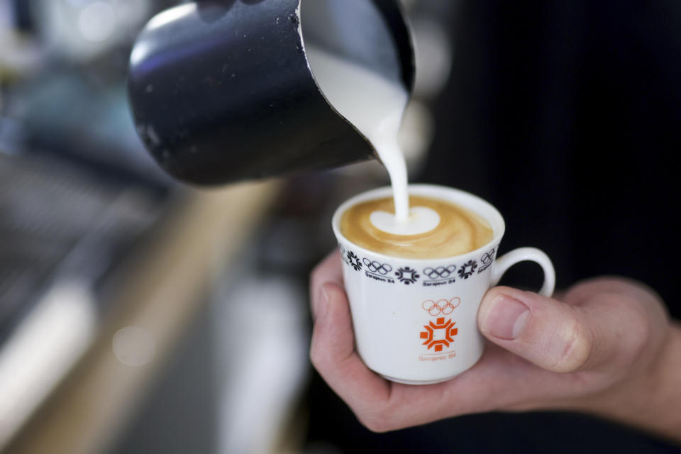 A bartender pours milk in a in coffee cup designed for the Sarajevo Olympic Games in a Kawa coffee shop in downtown Sarajevo, Bosnia, Monday, Feb. 5, 2024. Sarajevo is paying tribute this week to one of its most glorious moments: the two weeks of February in 1984 when it staged an impeccable Winter Olympic Games. While taking the nostalgic trip down memory lane, Bosnian Olympians say they are looking to the future with hope to again pull off an “apparently impossible feat” and reignite the Olympic flame over Sarajevo in 2032. (AP Photo/Armin Durgut)