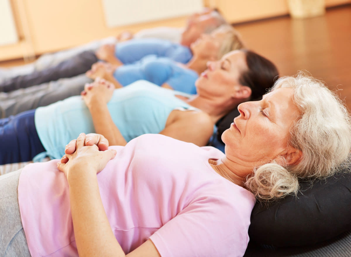 senior woman doing breathing exercise while lying down in mediation class