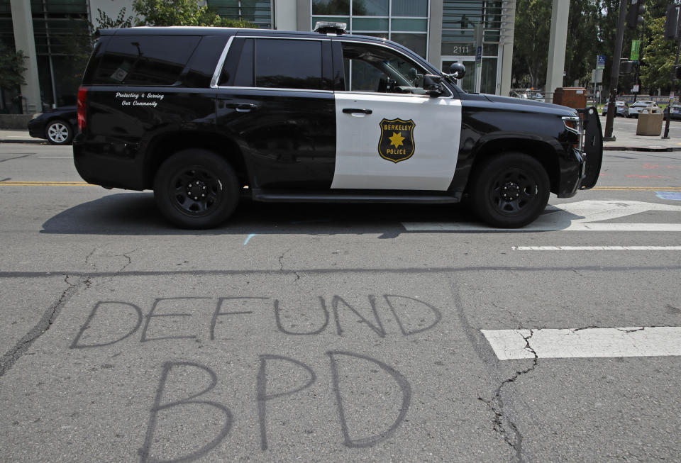 A Berkeley police vehicle waits at a stop light near graffiti calling for the defunding of the Berkeley police department on Wednesday, July 15, 2020, in Berkeley, Calif. The city of Berkeley moved forward Wednesday with a proposal to eliminate police from conducting traffic stops and instead use unarmed civilian city workers as part of a broad overhaul of law enforcement. The City Council also set a goal of cutting the police budget by 50%. (AP Photo/Ben Margot)