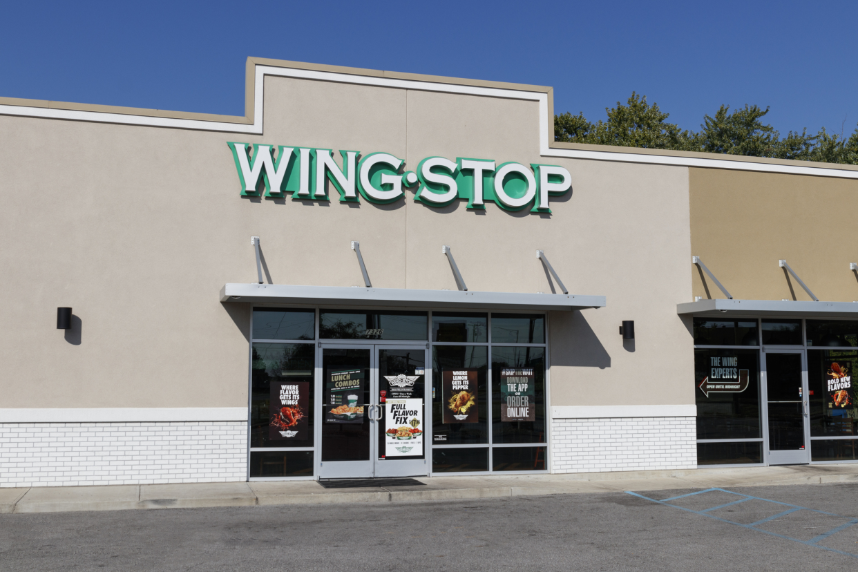 Front exterior of Wingstop, Indianapolis, front windows and doors with large light beige walls on both sides, front parking, against a blue sky