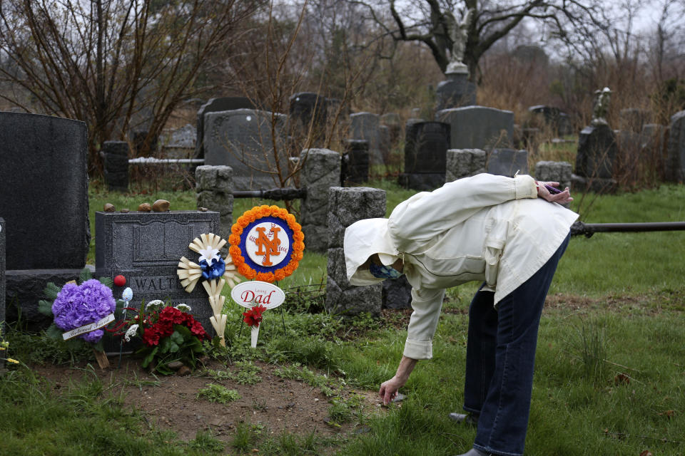 Peg Walter finds a rock to place on her late husband's headstone at All Faiths Cemetery in the Queens borough of New York, Sunday, April 11, 2021. John Walter died from the coronavirus May 10, 2020. (AP Photo/Jessie Wardarski)