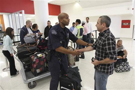 Nathan Lang (R) shakes hands with an airport police officer after picking up luggage he left in the food court while fleeing a shooting incident the previous day, just in time to make his connecting flight at Los Angeles airport (LAX), Los Angeles, California November 2, 2013. REUTERS/David McNew