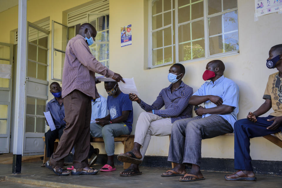 People receive consent forms as they wait to be vaccinated against the coronavirus at Aywee health center in the Gulu district of Uganda on Thursday, Sept. 23, 2021. Repeated and sudden power failures plague the vaccine storage unit, adding to the logistical challenges facing efforts to ramp up vaccination across the country. (AP Photo/Nicholas Bamulanzeki)