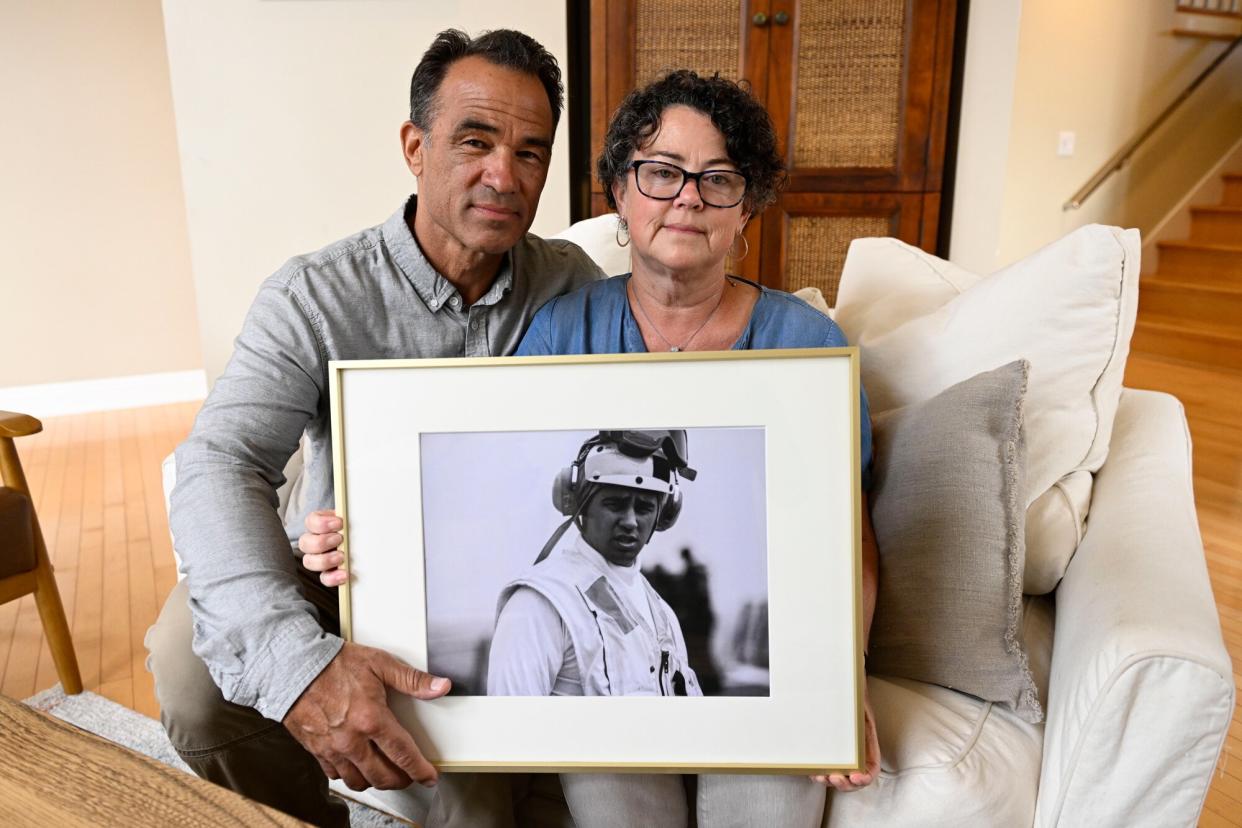 Derek and Suzi Alkonis pose with a photo of their son Lt. Ridge Alkonis on Wednesday, June 1, 2022, in Dana Point, Calif. Their son, a U.S. Navy lieutenant in Japan, faces a potential three-year prison sentence for a car crash that killed two people last year. The family of Alkonis says he suffered from acute mountain-sickness and passed out unconscious behind the wheel. Japanese prosecutors and a judge say he was feeling drowsy and should have pulled over.