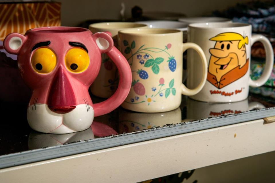 Pink panther, flower, and Barney Rubble mugs in a line on a shelf