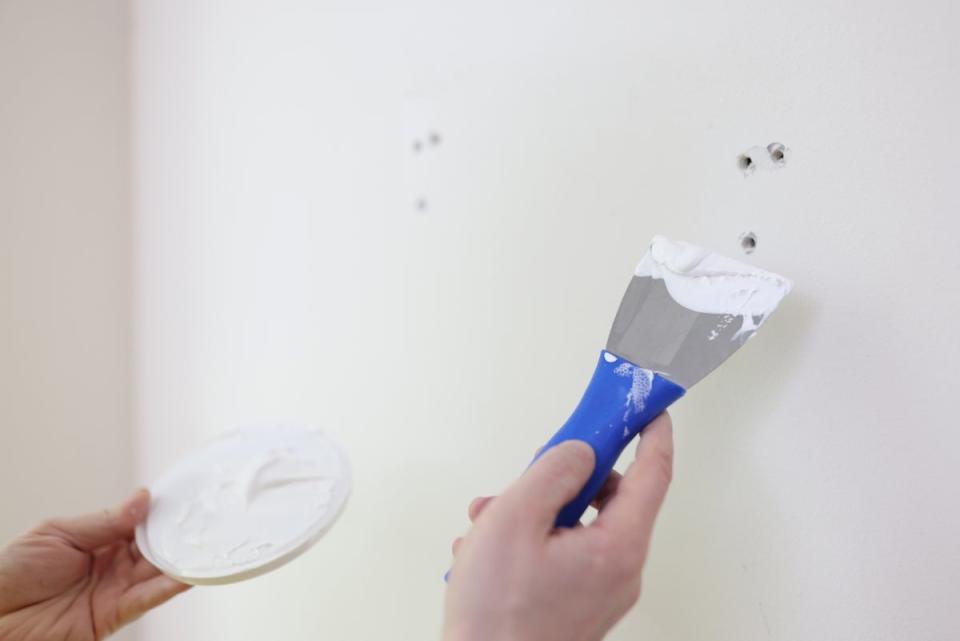 Person patching small holes in a wall with a putty knife.