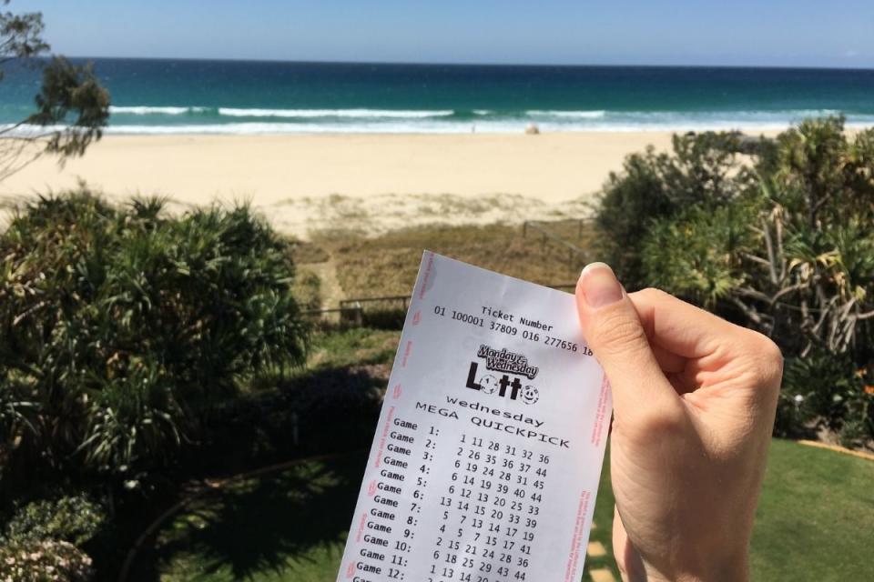 Hand holds up winning Lotto ticket at the beach. Source: The Lott