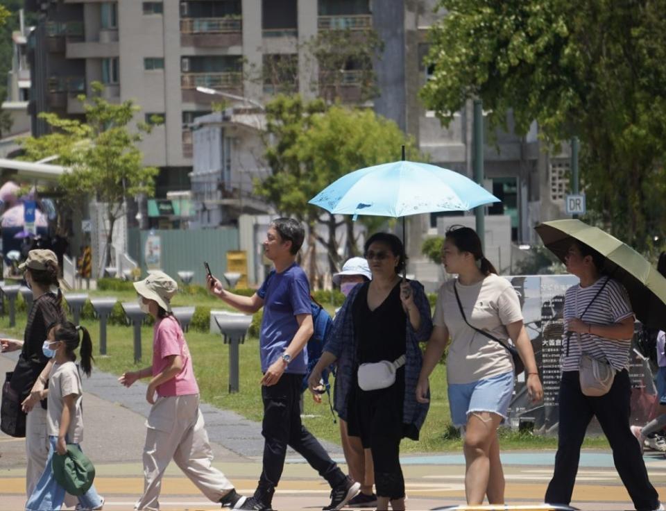 中央氣象署表示，23日各地多雲到晴，氣溫仍偏高，醫師提醒要做好防曬。圖為高雄市鹽埕區民眾撐傘、戴帽防曬。（中央社）