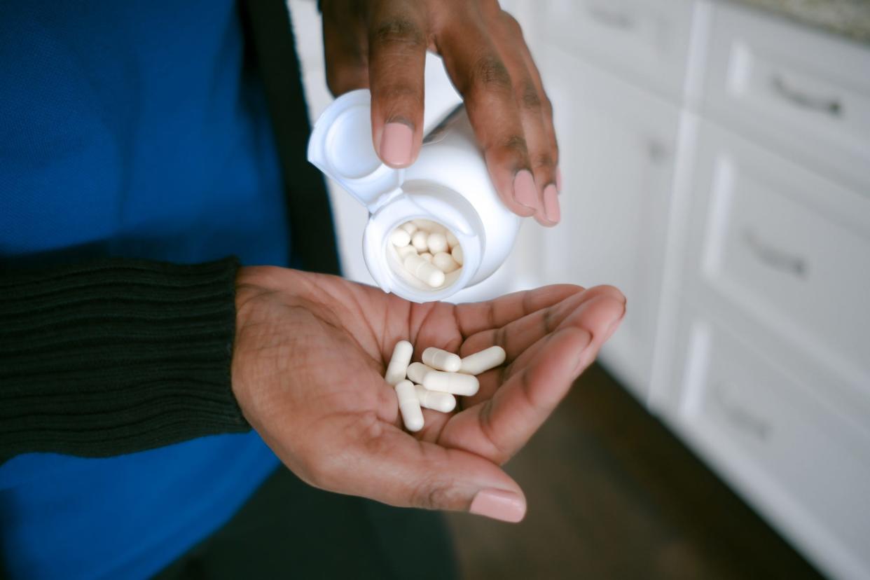 A person pours a white bottle filled with supplements into their palm.