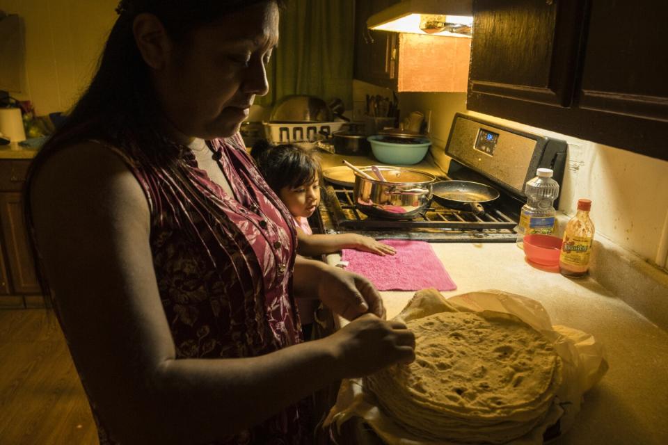 Enedina Ventura grabs a tortilla as daughter Judith Villegas watches a pot of soup in the kitchen