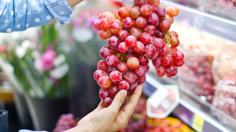 person picking fresh grapes at supermarket