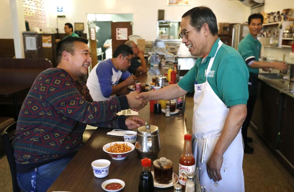 Frank Shyong shakes the hand of a restaurateur while seated at the dining bar