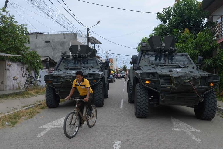 Un hombre pasea en bicicleta junto a vehículos blindados fuera de un centro de votación durante un referéndum sobre medidas más estrictas contra el crimen organizado en Olón, provincia de Santa Elena, Ecuador, el 21 de abril de 2024.