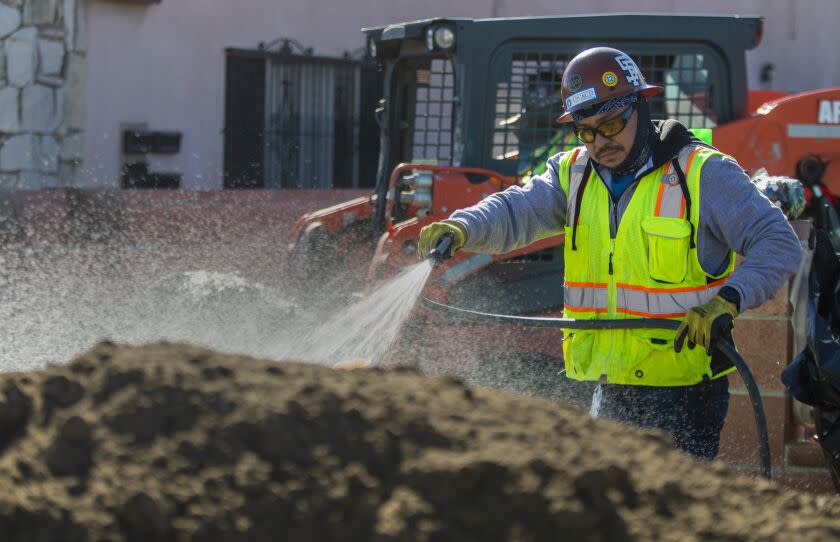 Maywood, CA - November 10: A worker spray water on a pile of contaminated soil before moving it on Thursday, Nov. 10, 2022, in Maywood, CA. Properties have dangerous amounts of lead in their soils after decades of being coated by pollution from a nearby lead-acid car battery smelter (Exide Technologies). The state has cleaned up about 4,000 properties within a 10,000-parcel area that was affected by this pollution. (Francine Orr / Los Angeles Times)