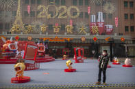 In this Tuesday, Jan. 28, 2020 photo, a man wearing a face mask walks through a Lunar New Year holiday display at a normally busy pedestrian shopping street in Beijing. Fears of a virus outbreak have kept many indoors and at home in China's capital. Cultural landmarks such as the Great Wall and Forbidden City have closed their doors to visitors, nearly deserted shopping malls have reduced their operating hours, and restaurants that remain open draw just a handful of customers. (AP Photo/Mark Schiefelbein)