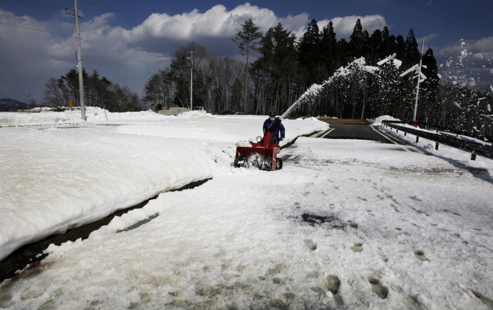 In this Monday, March 3, 2014 photo, a worker removes snow left on an access road at a construction site for housing March 11, 2011 tsunami survivors who lost their homes in Tanohata, Iwate Prefecture, northeastern Japan. In Tanohata, as in many other cities and towns laid waste by the mountain of water that scoured their scenic harbors, groundwork has just finished for a fraction of the many homes due to be built, with construction not yet started. (AP Photo/Junji Kurokawa)