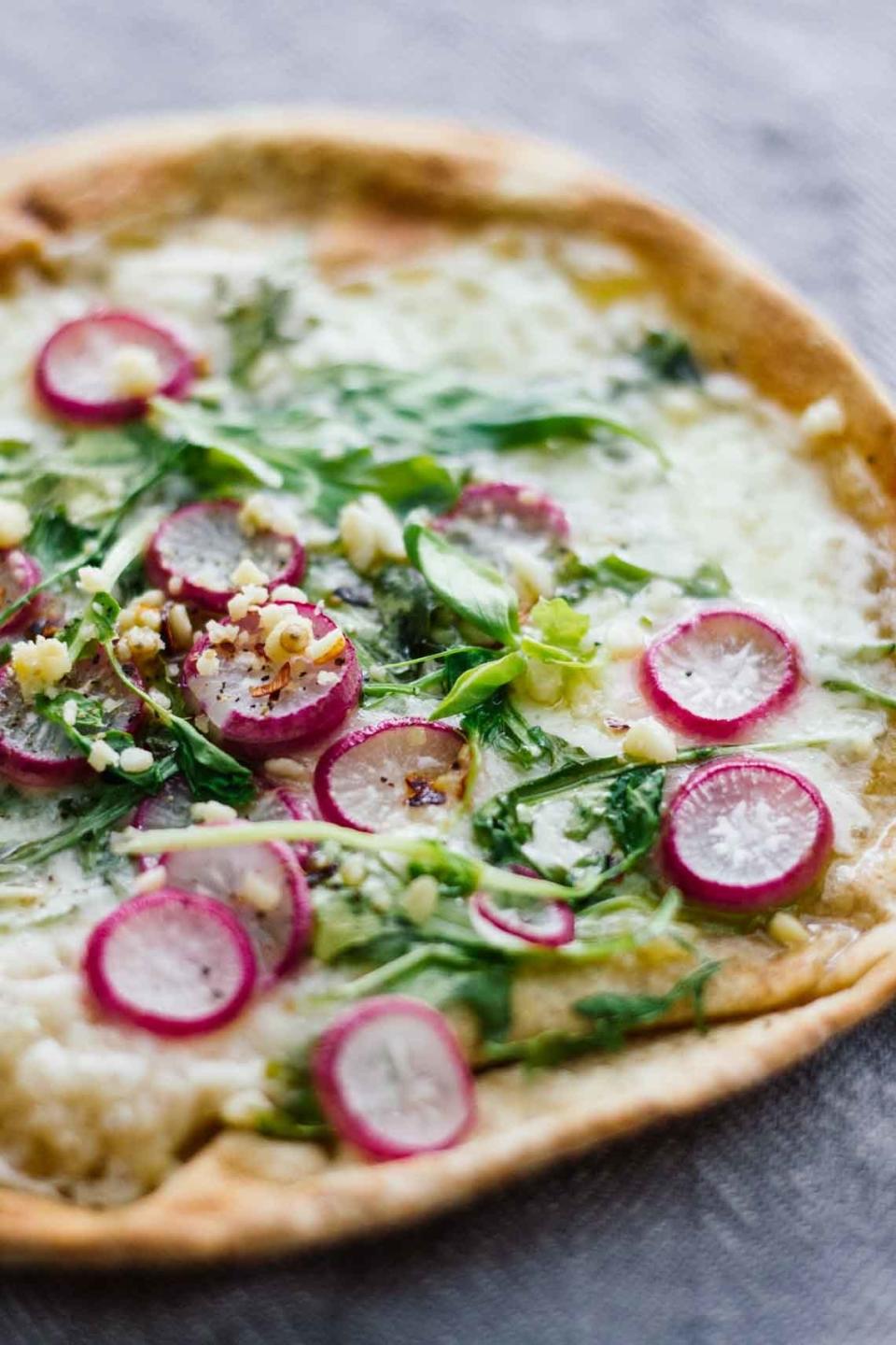 A pita pizza topped with cheese, radish, and arugula.