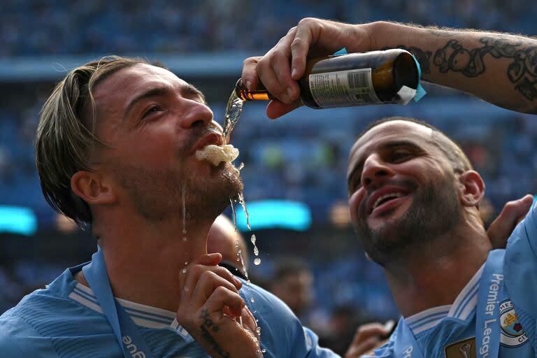 El defensor inglés del Manchester City #02 Kyle Walker (derecha) vierte cerveza en la boca del centrocampista inglés del Manchester City #10 Jack Grealish mientras celebran por el título de la premier League ganado este domingo