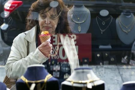 A woman eats ice cream as she looks at the display in the window of a Gold Standard jewellery store that specializes in purchasing raw gold and silver in New York April 15, 2013. REUTERS/Lucas Jackson