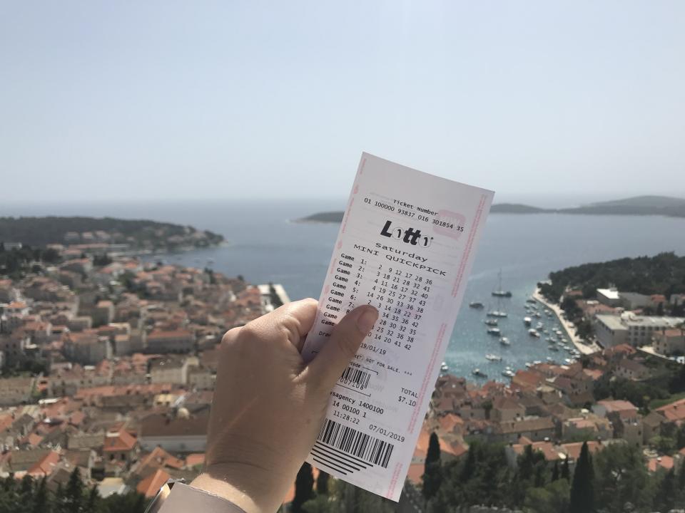 A person holds a Saturday Lotto ticket while overlooking the ocean.