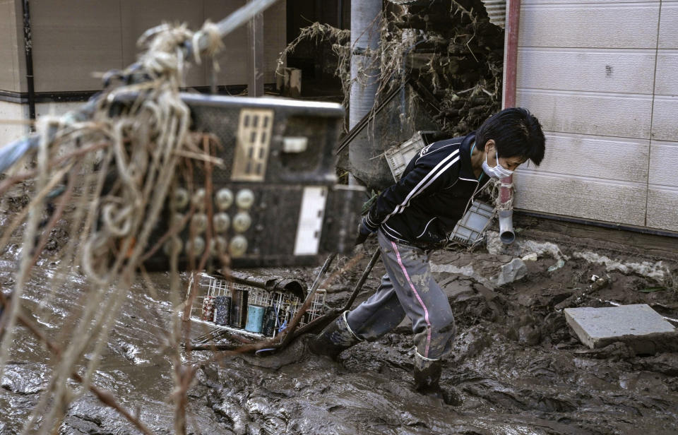 A woman makes her way though the mud and debris from Typhoon Hagibis, with a phone hanging on the wire, front, at Hoyasu district in Nagano, central Japan Wednesday, Oct. 16, 2019. The typhoon hit Japan's main island on Saturday with strong winds and historic rainfall that caused more than 200 rivers to overflow, leaving thousands of homes flooded, damaged or without power. (Koji Sengoku/Kyodo News via AP)